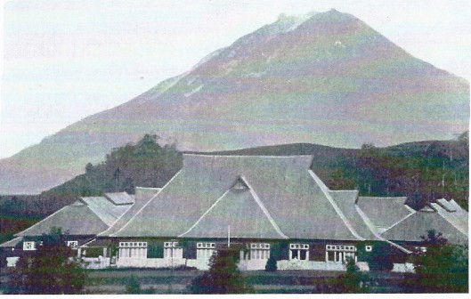 Het hoofdgebouw van de Planters School Vereniging (PSV) in Brastagi. Links enn rechts de twee afdelingen, elk met vier slaapzalen. Op de achtergrond de berg Sinaboeng