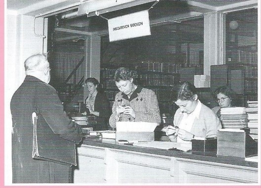 Rechts vooraan achter de uitleenbalie docente mej. Ans Schonebaum in de tijd dat zij nog werkte bij de openbare leeszaal en bibliotheek van Amsterdam in 1952